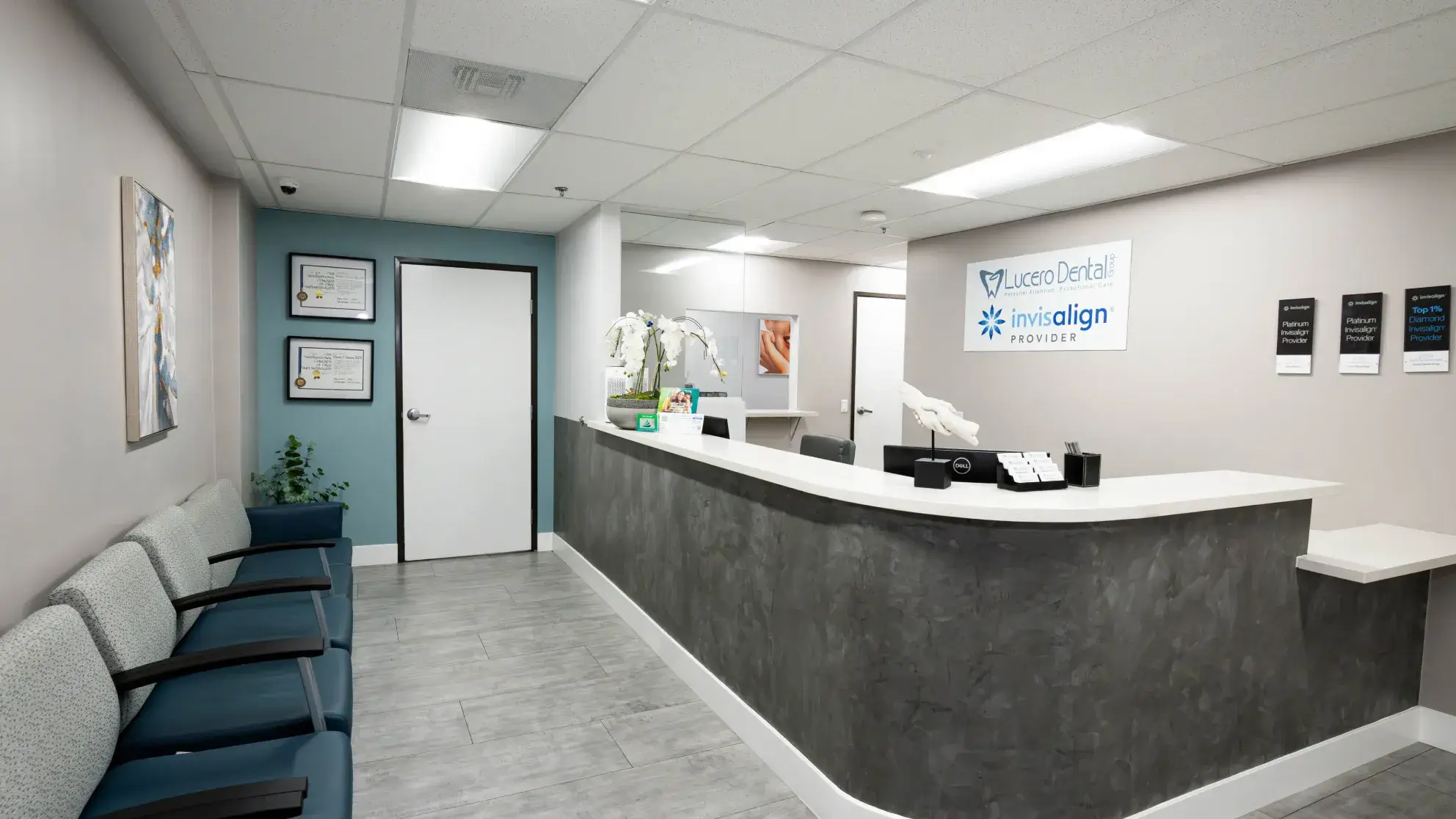 Modern dental office reception with gray countertop, waiting area chairs, and Lucero Dental Group Invisalign provider signs on the wall.