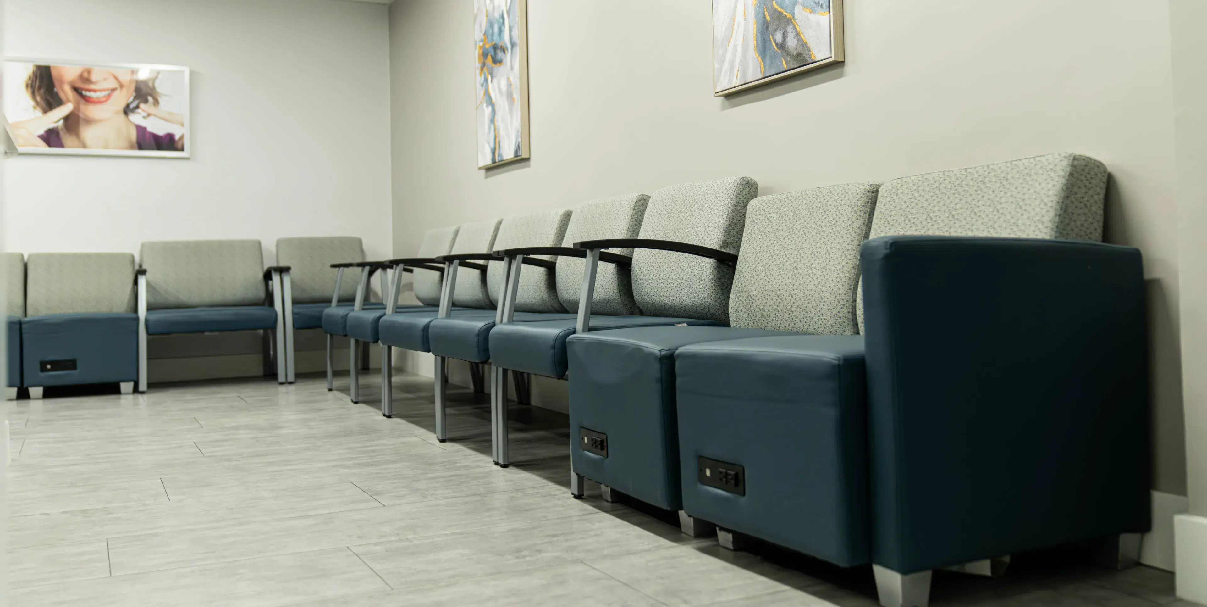 Row of blue and gray cushioned chairs with armrests in a clean waiting room featuring artwork on the walls.