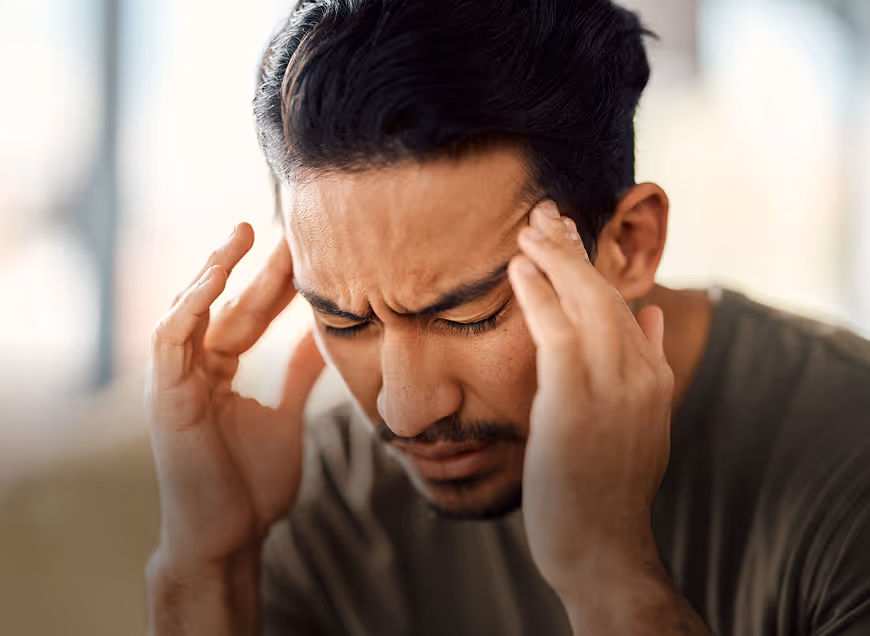 Young man with closed eyes holding his temples, appearing to have a headache or stress.