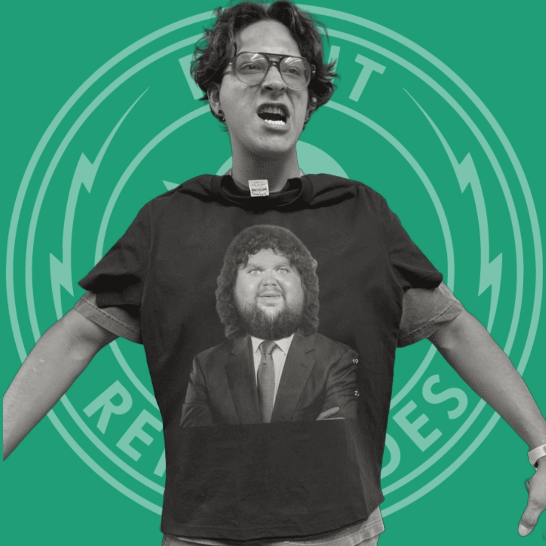 Person wearing glasses and a black t-shirt with a caricature of a man in a suit with a large head and beard, on a green background with a circular logo.