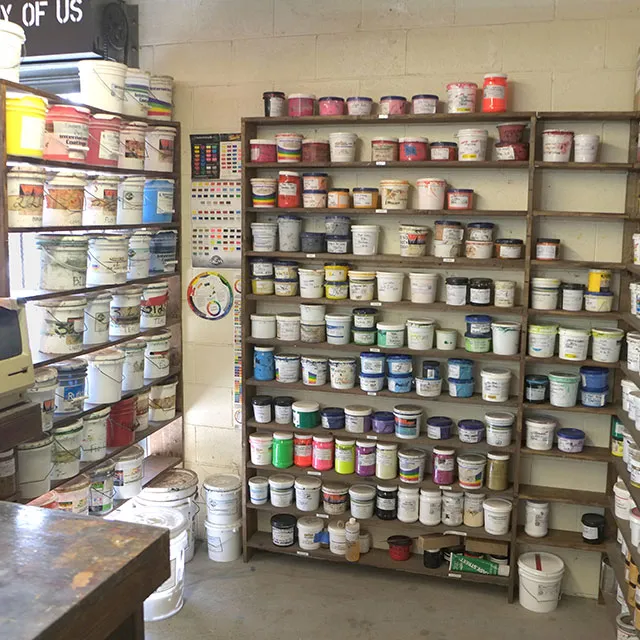 Shelves filled with various paint containers and buckets in a storage or workshop room.