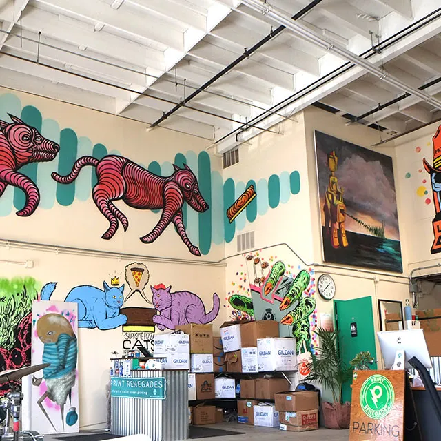 Interior of an art studio with colorful murals of striped dogs, blue and purple cats, and various paintings on the walls above stacked boxes.