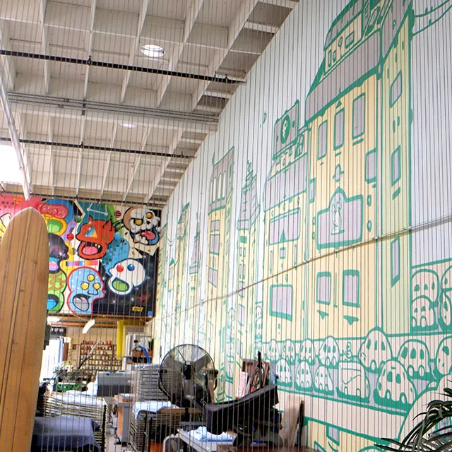 Interior view of a spacious, high-ceilinged room featuring a large mural with cartoonish skulls and colorful abstract faces on one wall, and a tall mural of simple city buildings with trees on another wall.