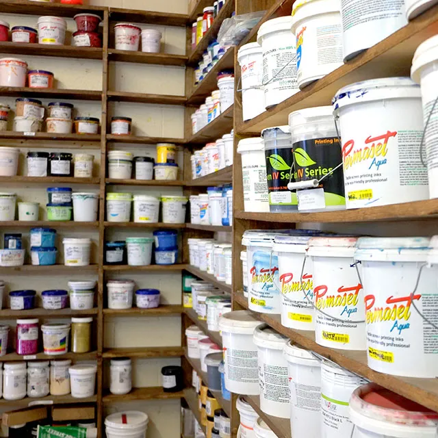 Shelves filled with various white plastic buckets and containers of printing inks and paints in a storage room.