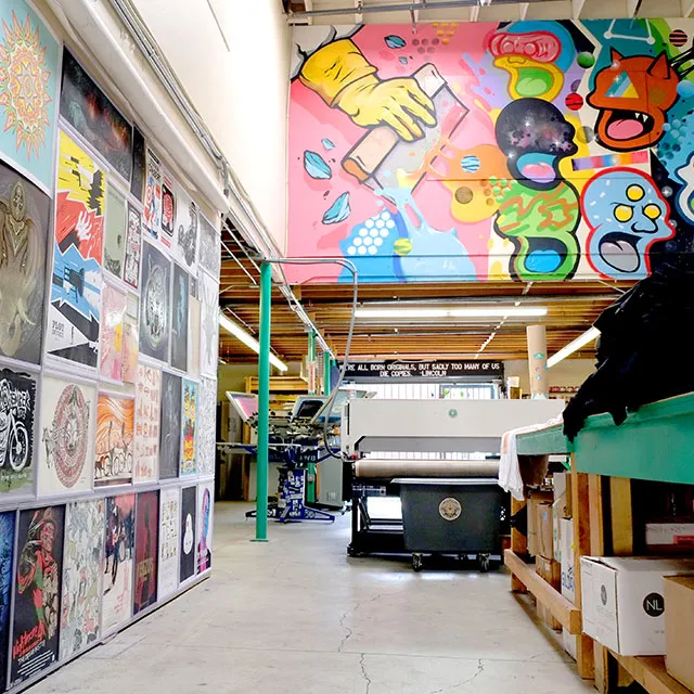 Interior of a vibrant art studio with colorful graffiti on the upper wall and various artworks displayed on the left wall.