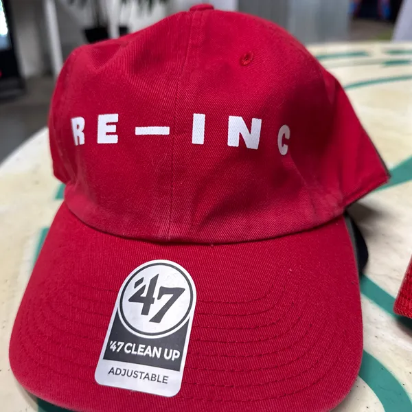 Red adjustable dad hat with the text 'RE-INC' printed in white on the front and a '47 CLEAN UP' label on the brim.