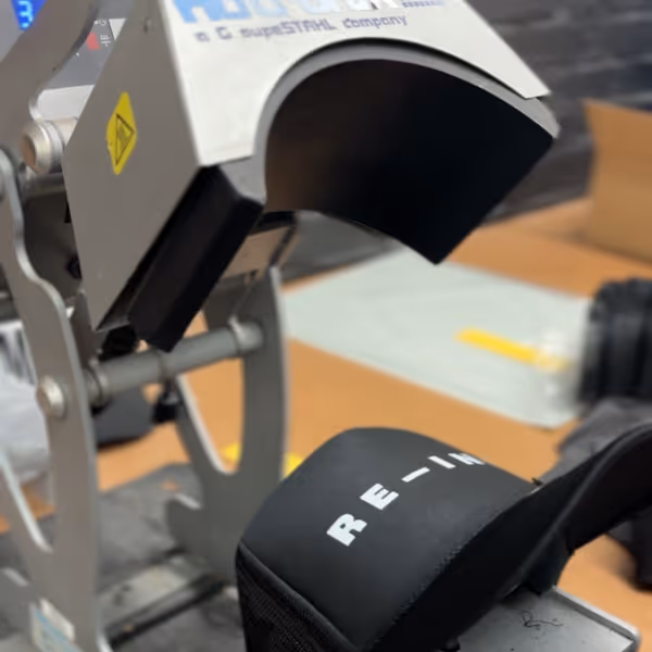 Close-up of a heat press machine applying a design on a black fabric with white text.