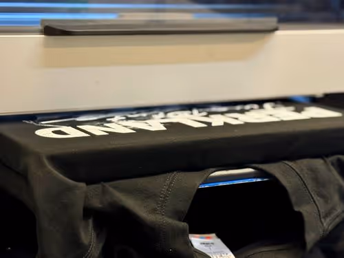 Close-up of a black t-shirt being printed with white text on a DTG printer.
