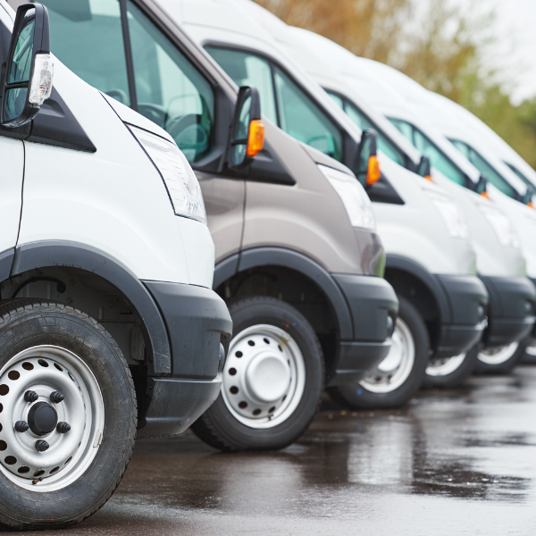 Row of white and gray delivery vans parked on wet pavement.
