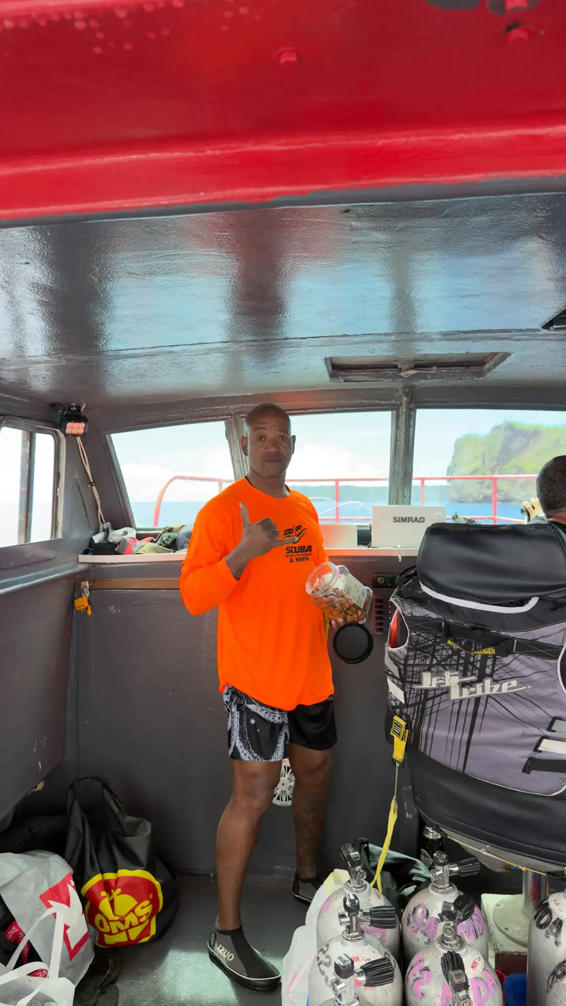 GAO Pacific Mission boat crew member throwing a shaka sign inside the vessel cabin alongside scuba diving equipment in Guam.