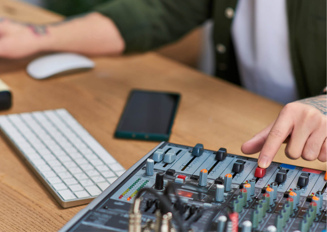 Close up of a man sitting at his desk, adjusting a sound board whilst using the computer
