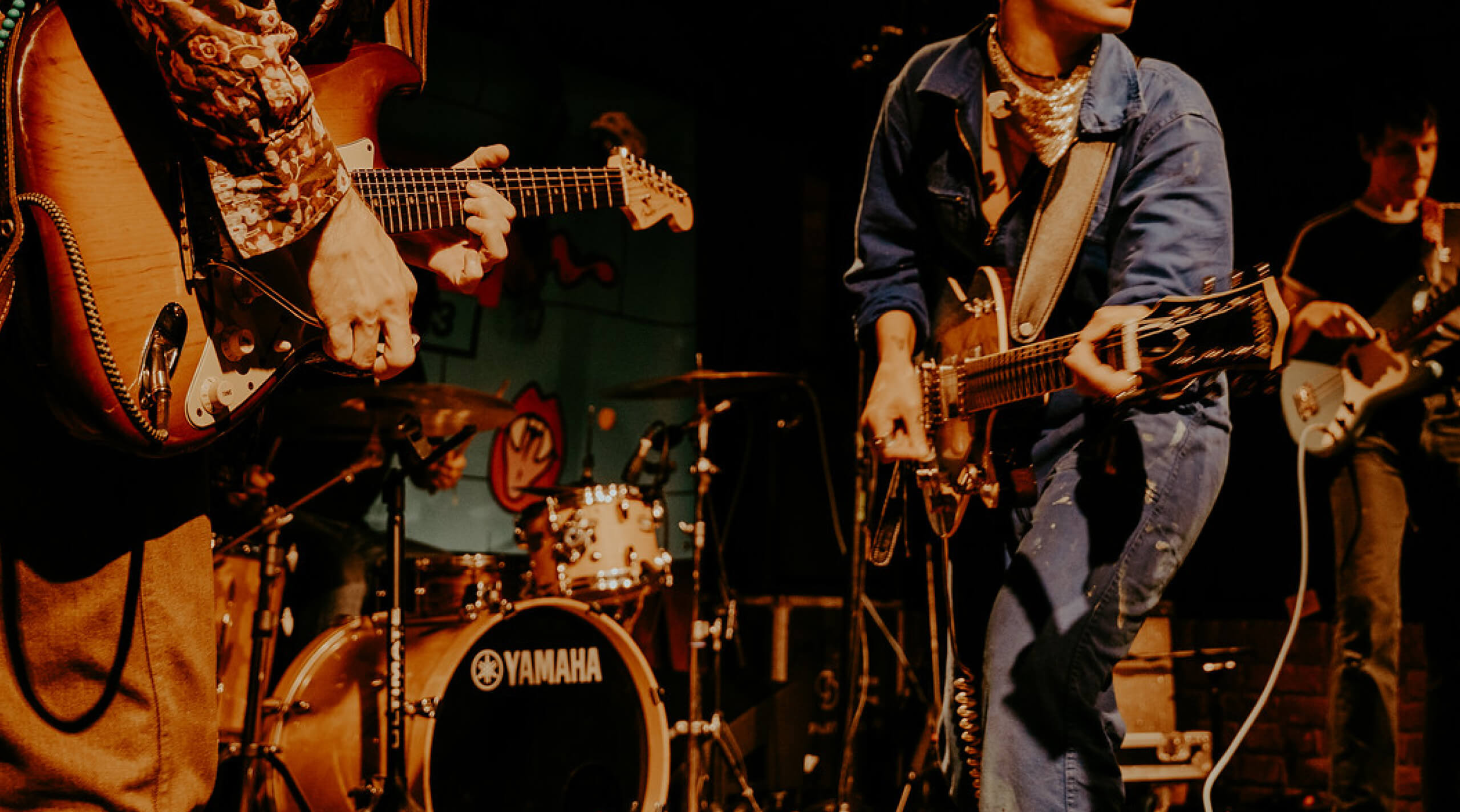 Three guitar and bassists in a band performing on a live stage