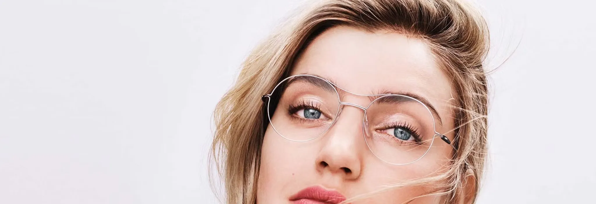 Close-up of a woman with blonde hair wearing thin, round silver eyeglasses and looking at the camera.