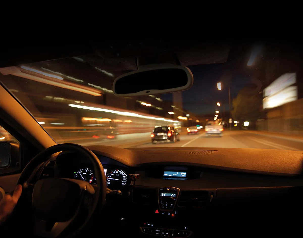 View from inside a car driving at night on a city street with blurred lights and other vehicles ahead.