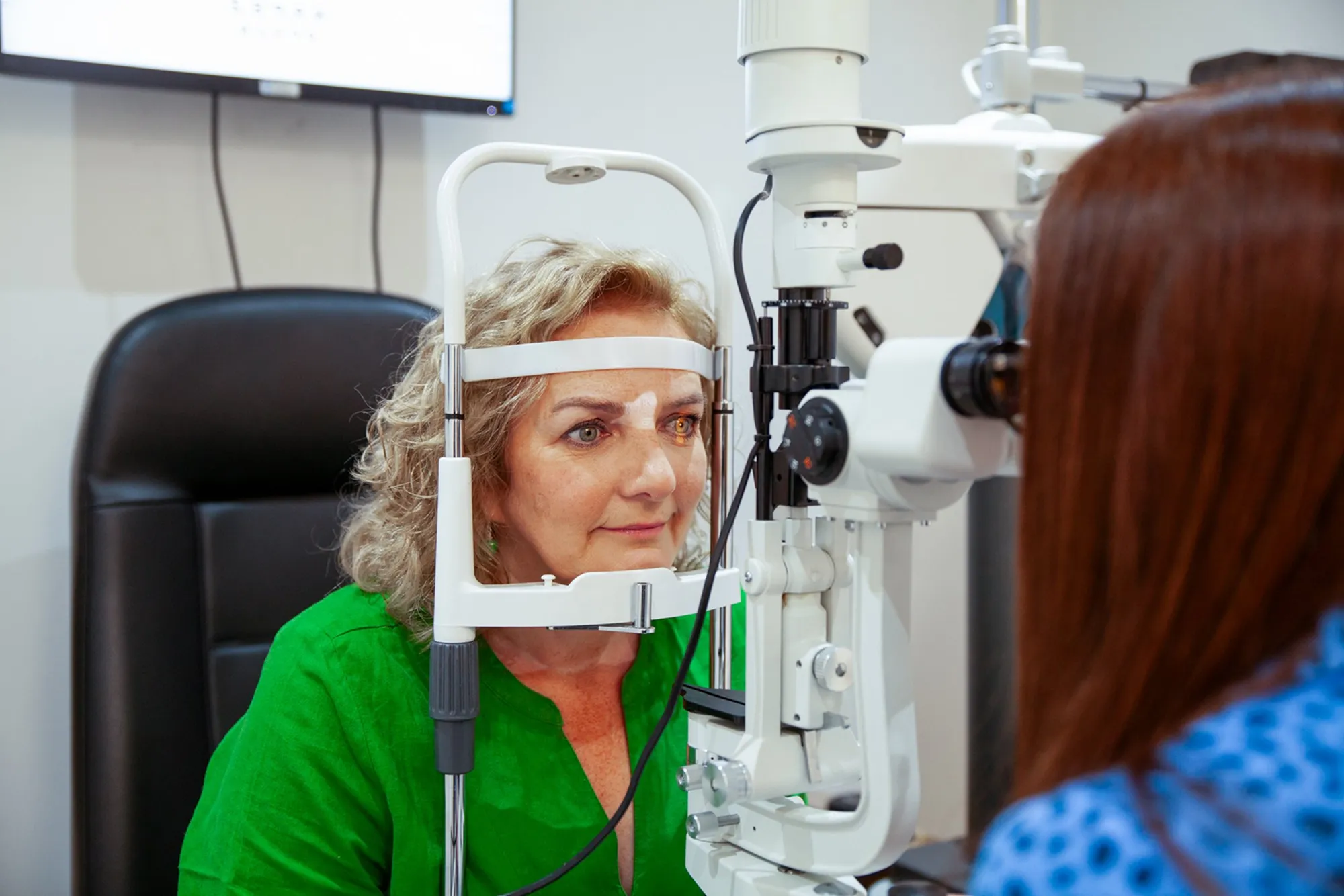 Middle-aged woman undergoing eye examination with a slit lamp at the optometrist's office.