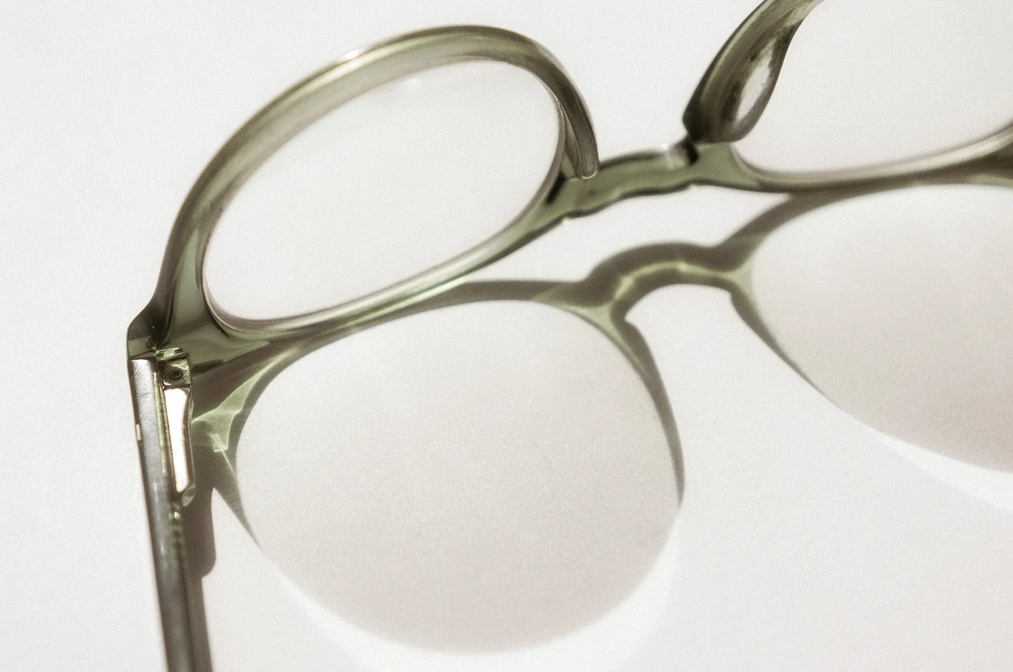 Close-up of round, translucent eyeglass frames casting shadows on a white surface.