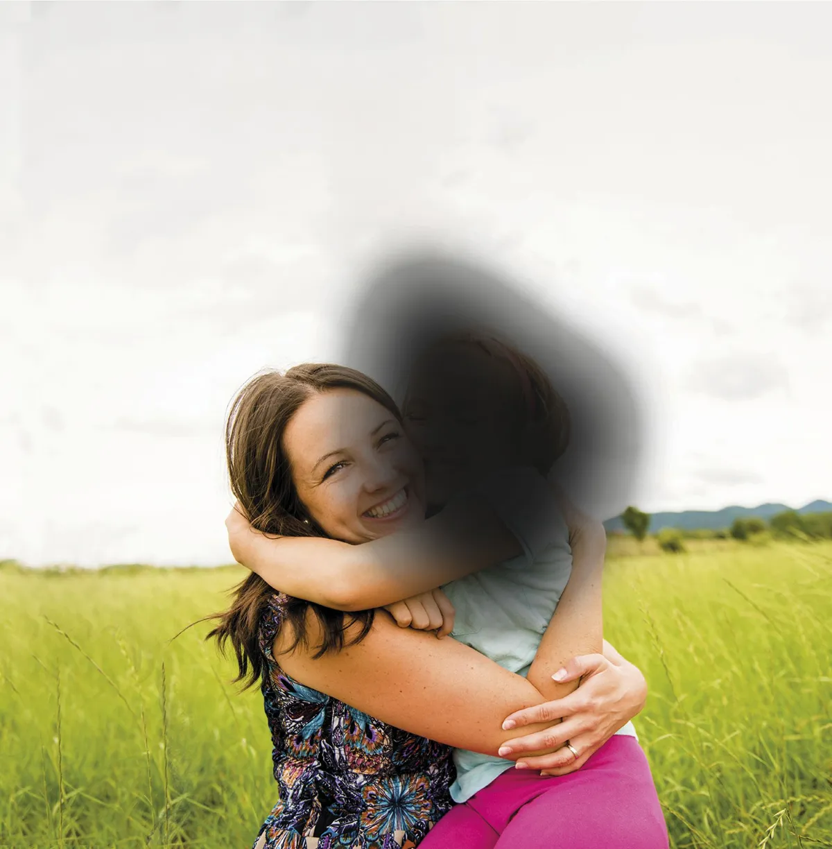 Woman hugging a child in a green field with mountains.