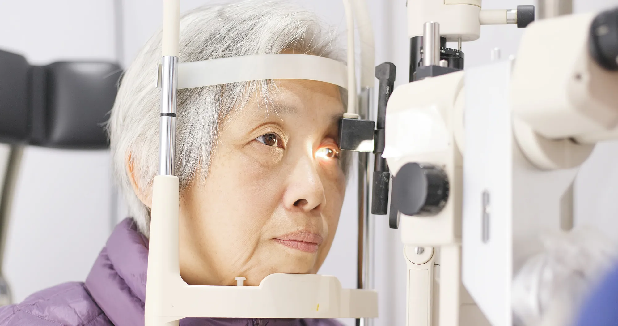 Senior woman undergoing an eye exam with a slit lamp in a clinical setting.