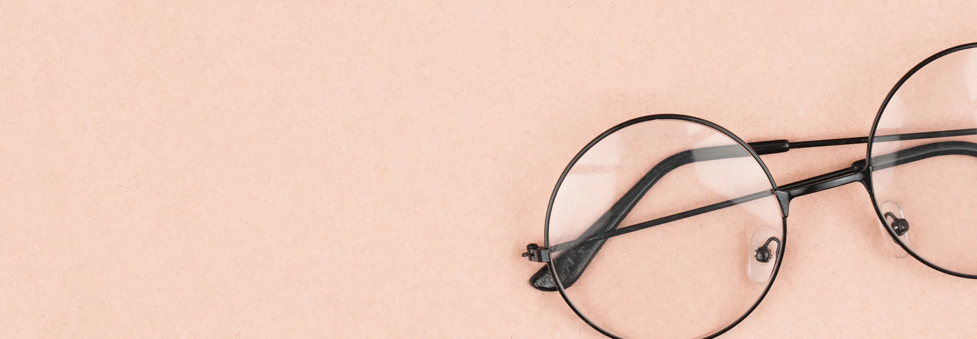 Round black-framed eyeglasses with clear lenses on a light peach background.