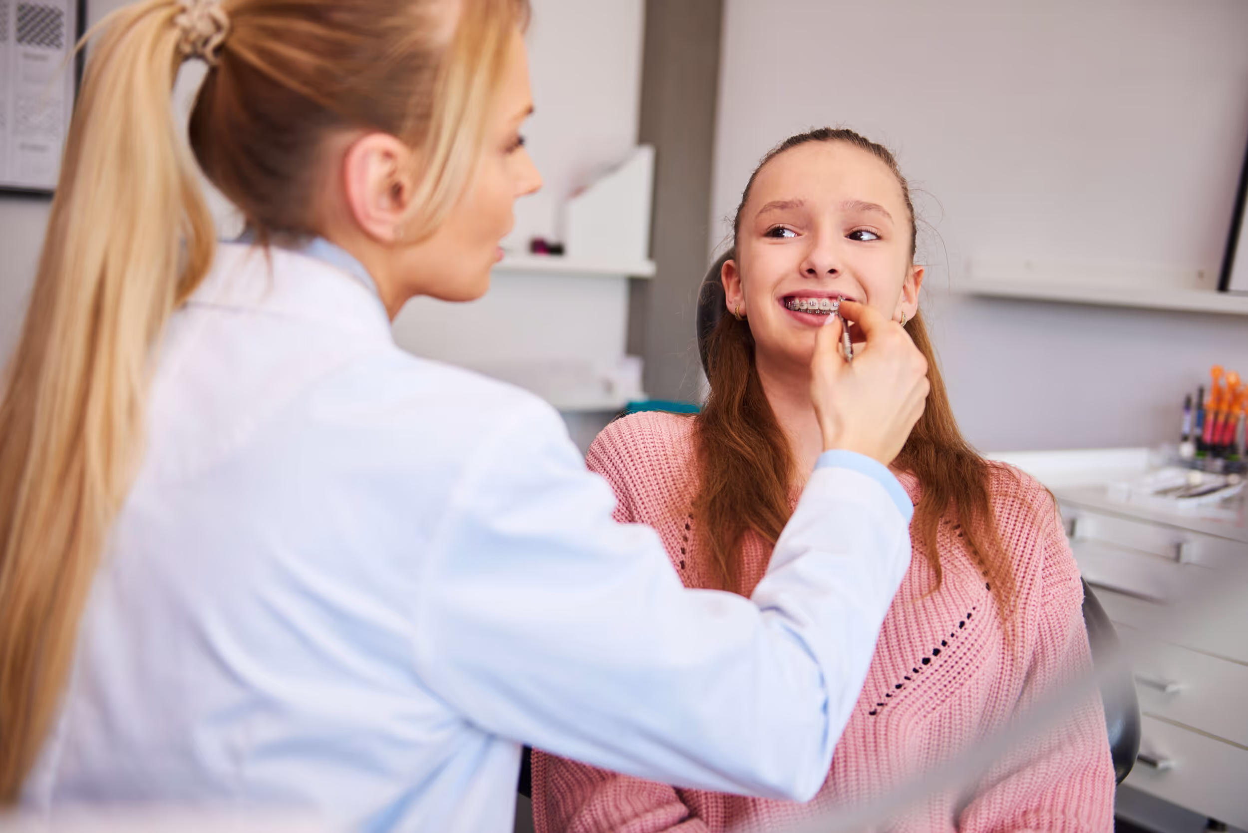 Orthodontist adjusting metal braces on a smiling teenage girl's teeth in a dental clinic.
