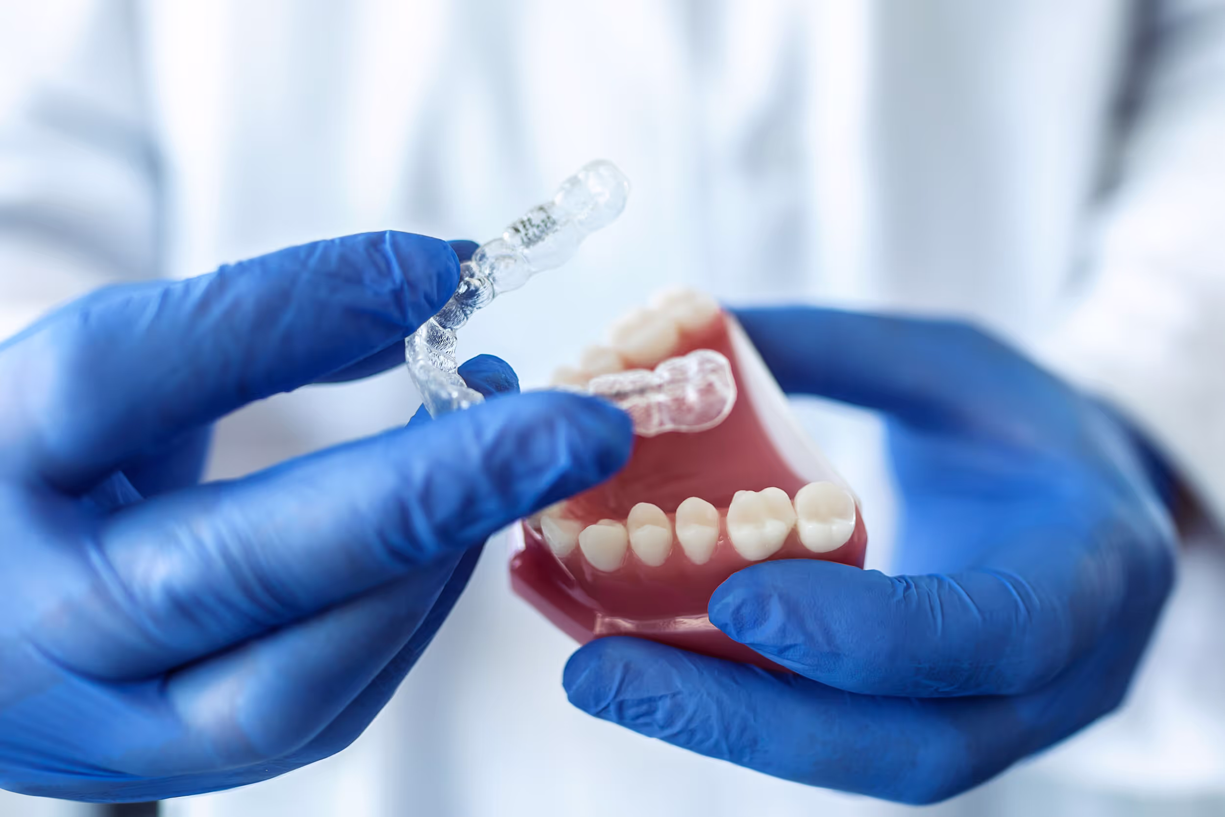 Gloved hands holding a dental model and a clear orthodontic aligner.