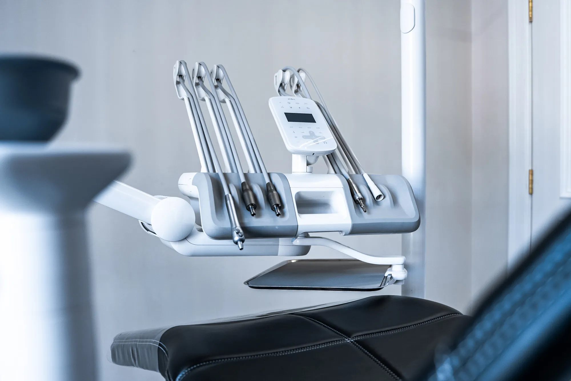 Close-up of dental equipment with multiple handpieces attached above a black dental chair.