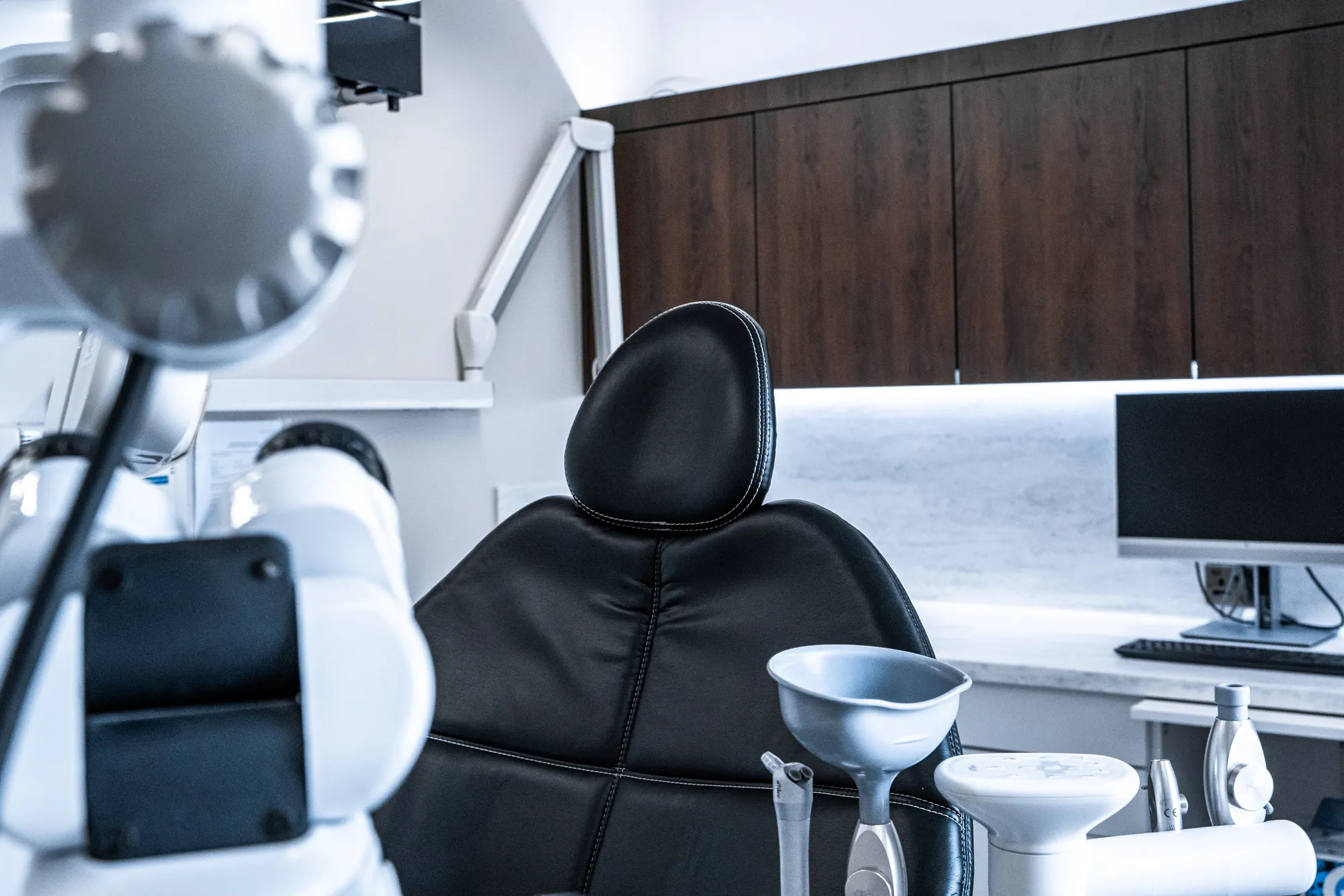 Black leather dental chair in a modern dental office with equipment and computer monitor in the background.