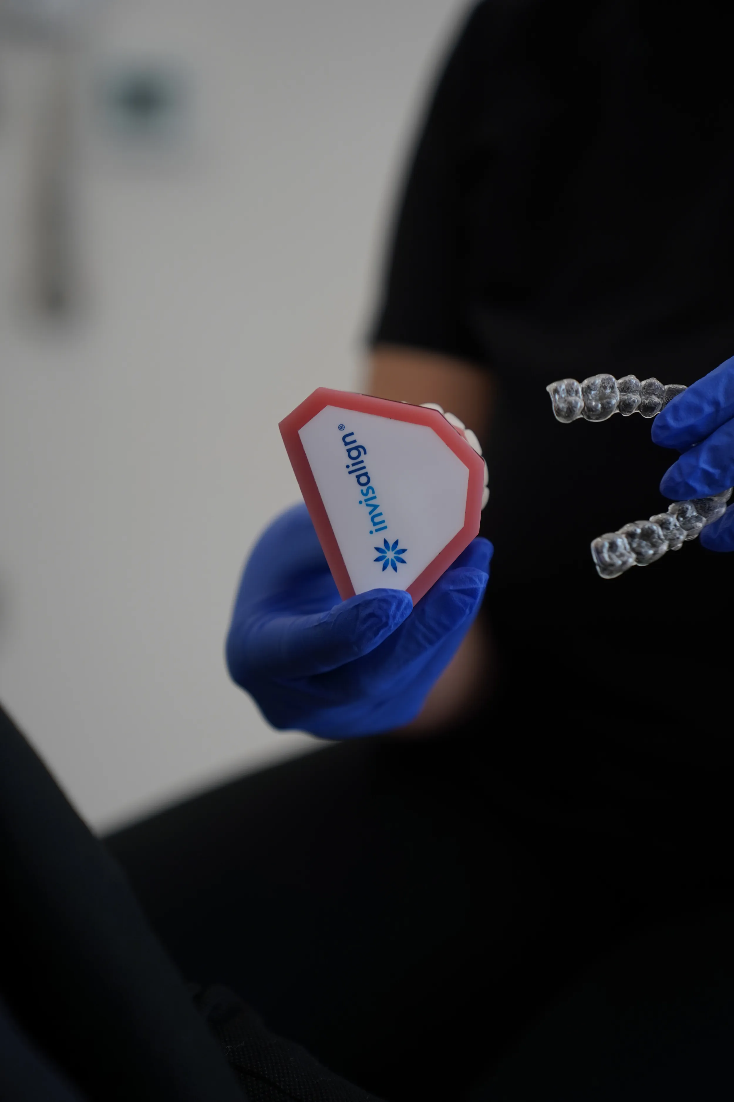 Person wearing blue gloves holding a clear Invisalign aligner and an Invisalign branded case.