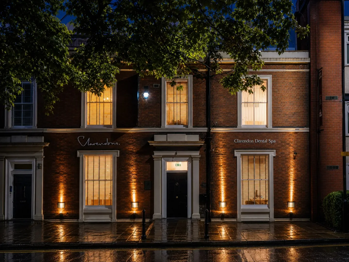 Exterior of Clarendon Dental Spa building at night with warm window lights and wet sidewalk.