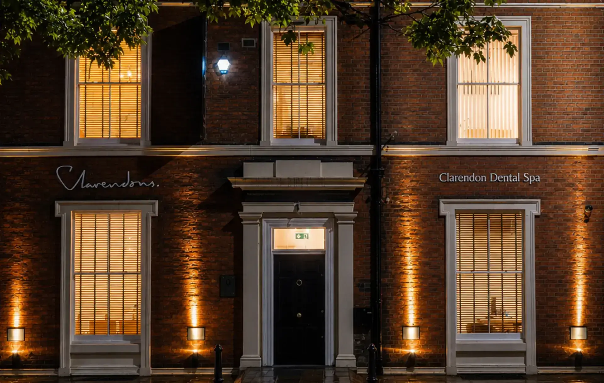Exterior of Clarendon Dental Spa building at night with warm window lights and wet sidewalk.