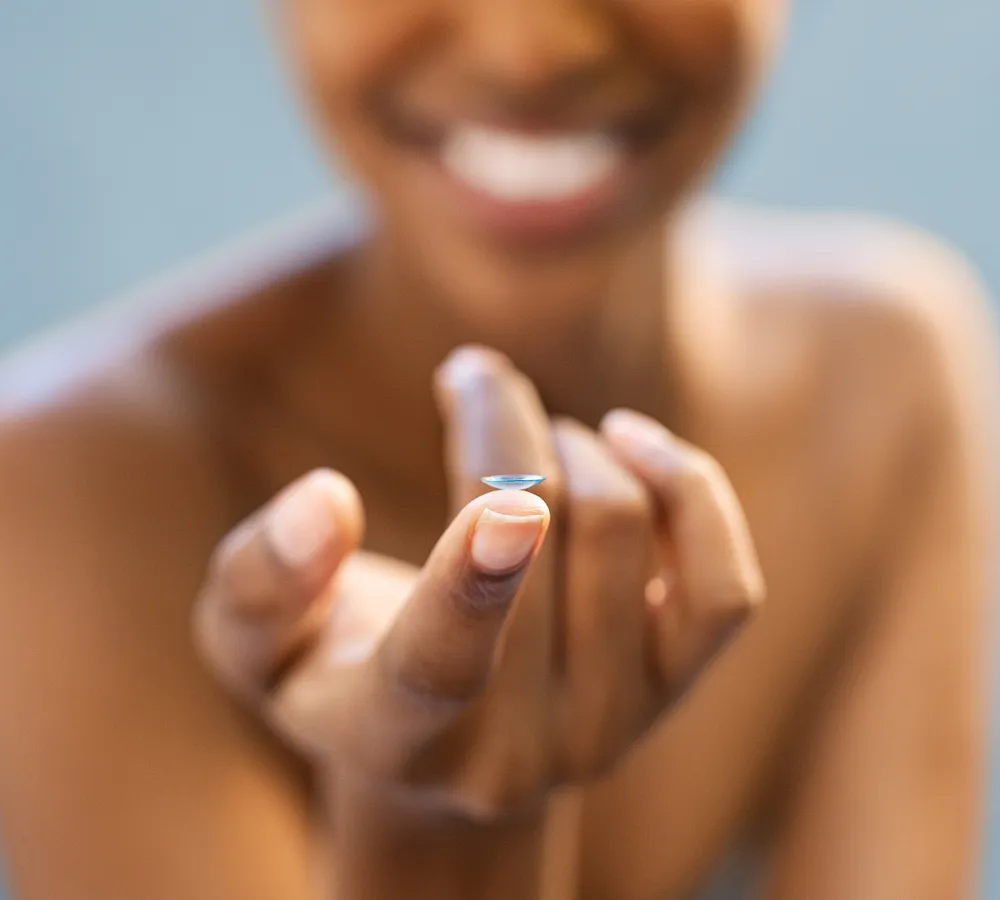 Smiling woman holding a contact lens on her fingertip.