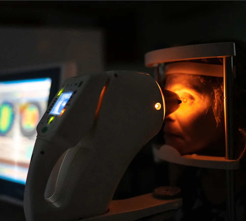 Person undergoing an eye exam with a retinal scanner emitting orange light in a dark room.