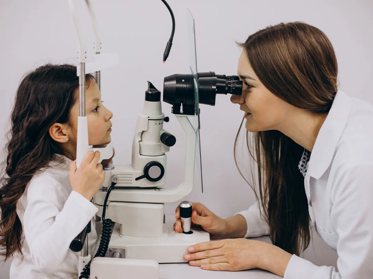 Young girl undergoing an eye exam with an ophthalmologist using a slit lamp device.