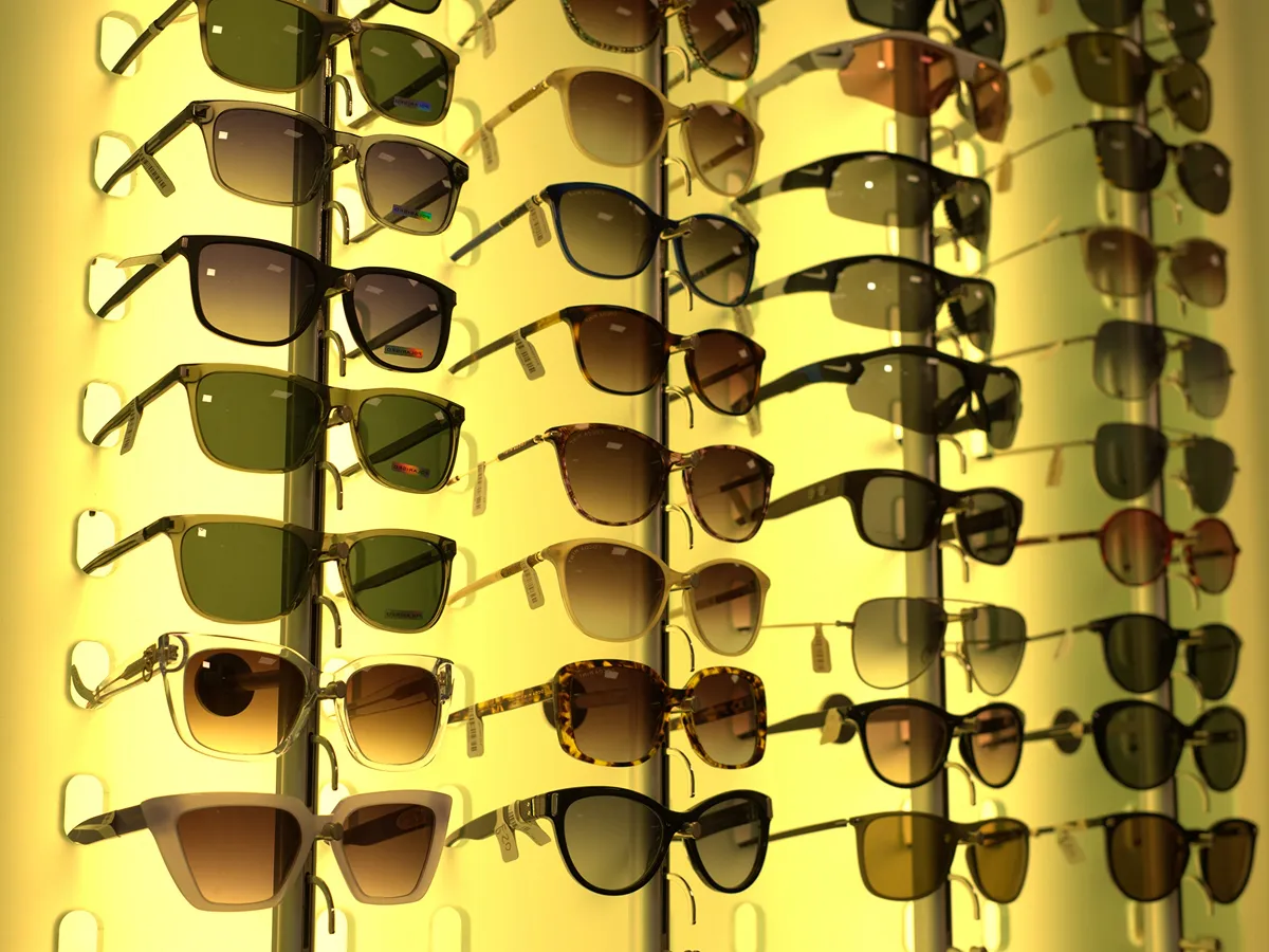 Multiple rows of varied sunglasses displayed on illuminated yellow shelves in an optometrist store.