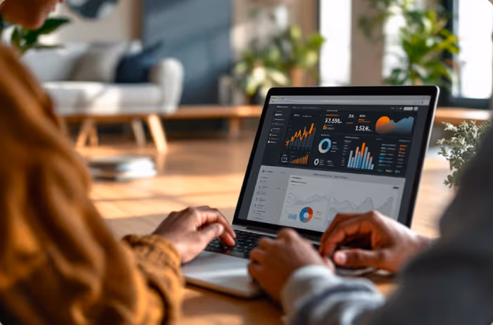Two people sitting at a table working on a laptop displaying colorful graphs and data analytics on the screen.