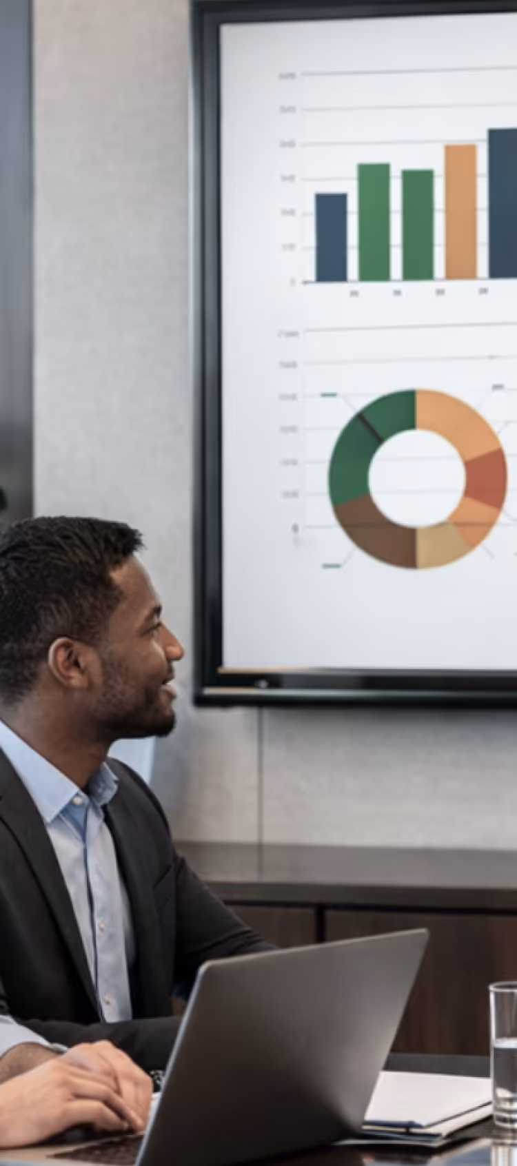 Man in a suit looking at a screen displaying bar and donut charts during a business meeting.
