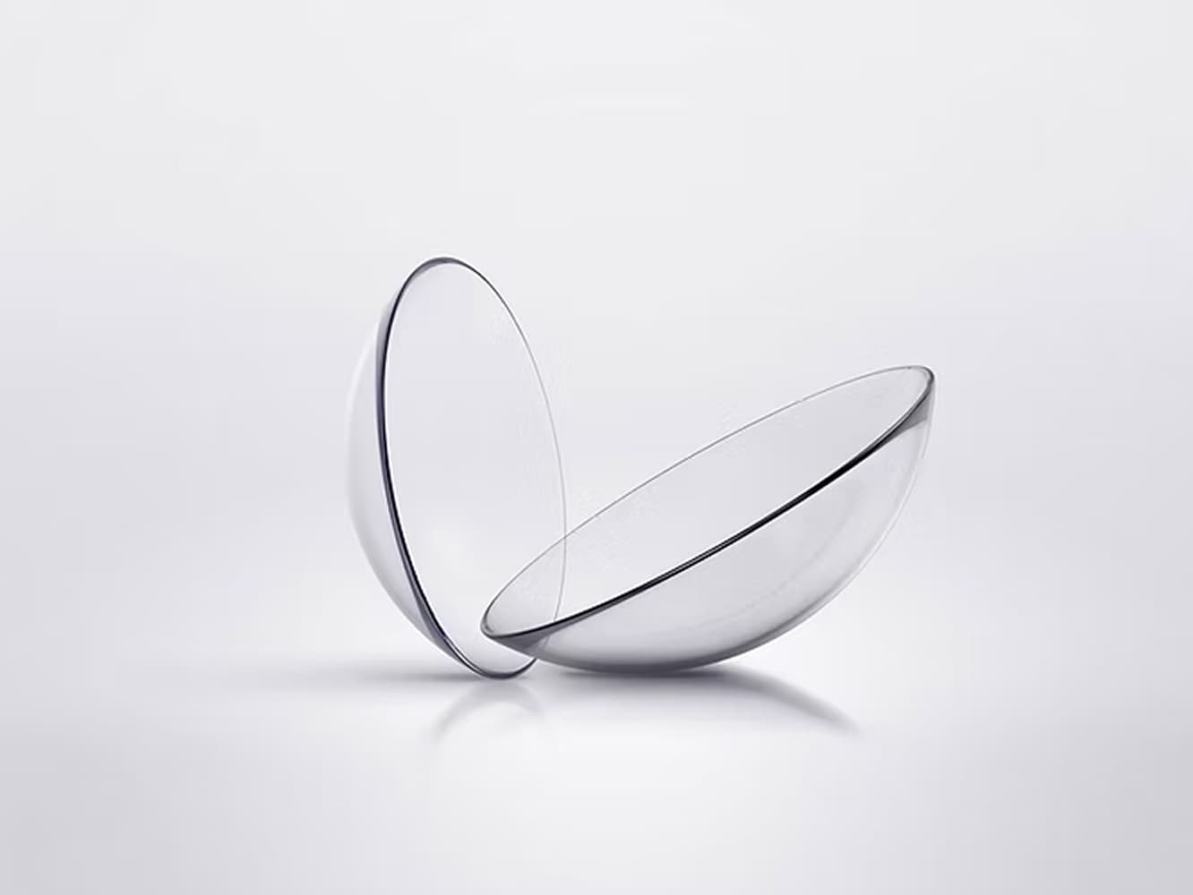Two transparent contact lenses positioned upright and leaning against each other on a smooth surface.