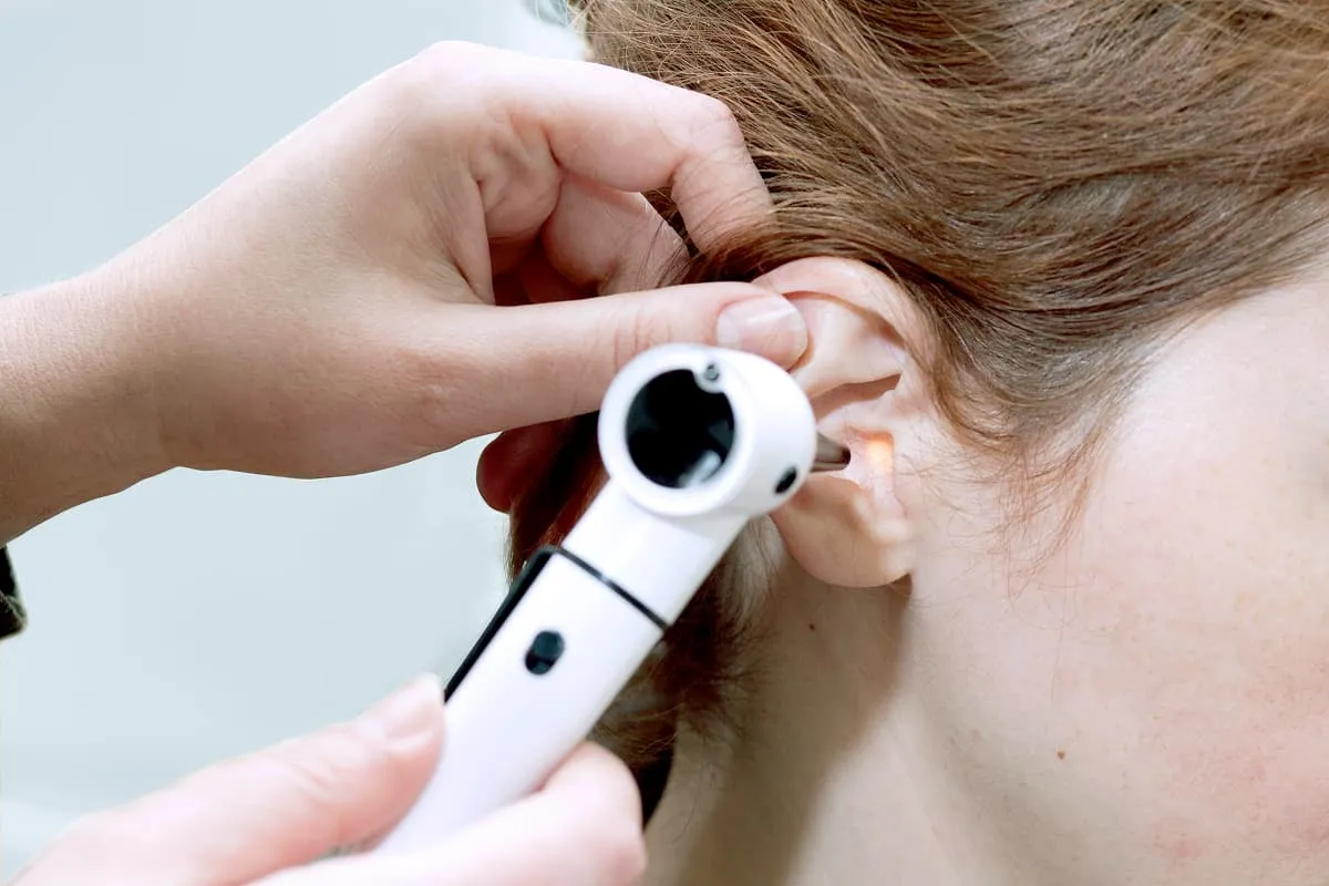 Medical professional using an otoscope to examine the ear of a person with light brown hair.
