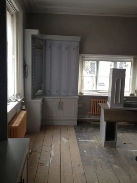 Room with large windows, light wooden floor, white cabinets, and a radiator under the window.