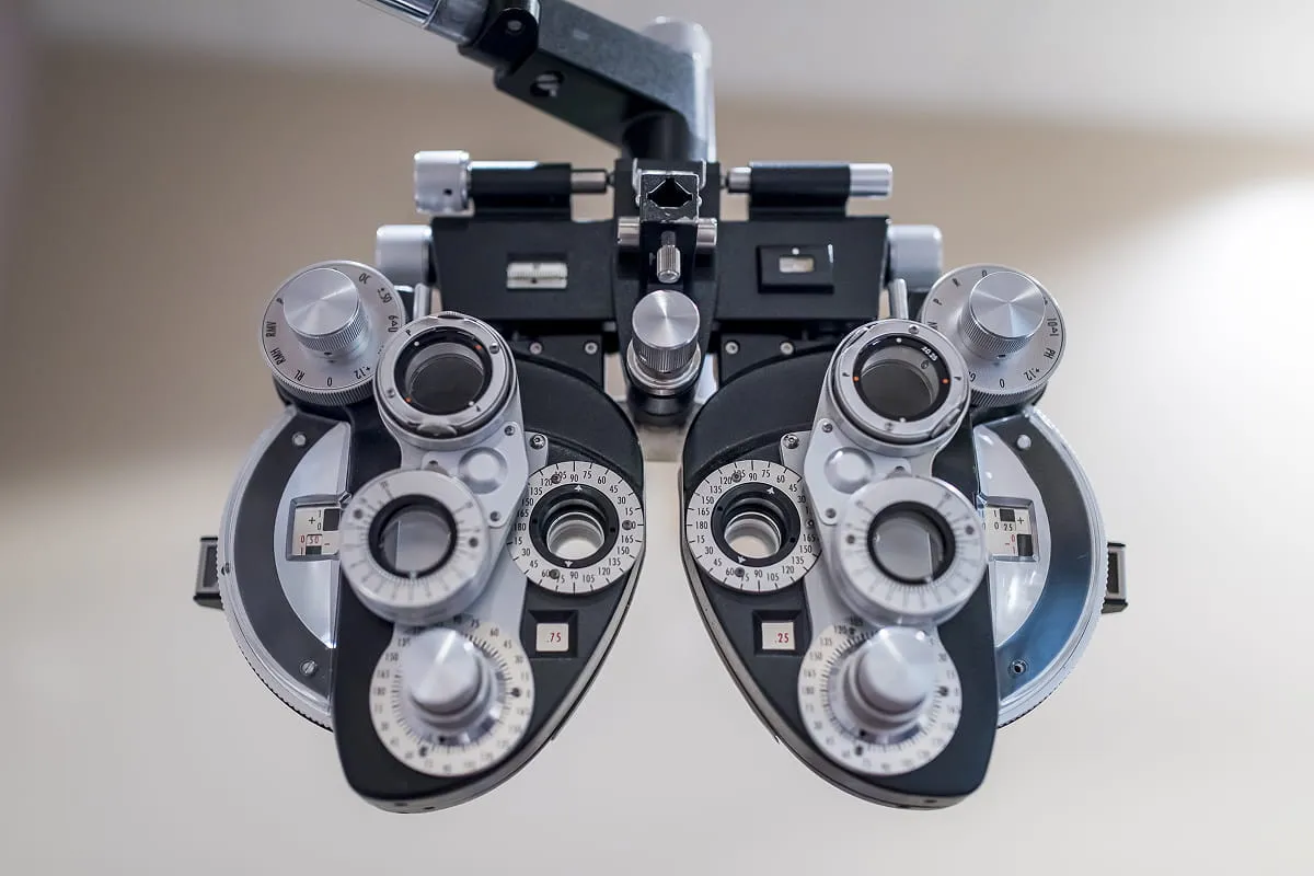 Close-up of an optometry phoropter device with multiple dials and lenses used for eye exams.