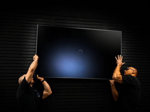 Two installers lifting a commercial display into position on a wall