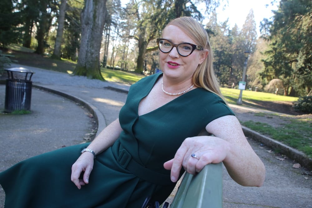 Photo of Nicole in a dark green dress, smiling  on a park bench in Portland.