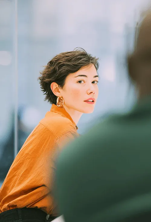 A woman in an orange top sitting at her desk in a meeting