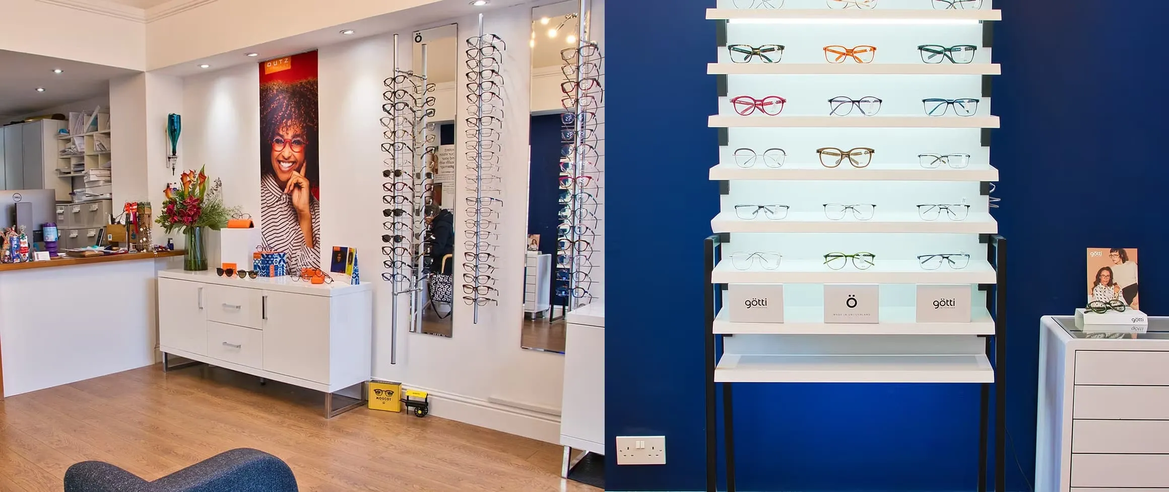 Interior of an optician’s shop with white display shelves holding multiple pairs of eyeglasses against a blue wall, a white cabinet with flowers and sunglasses, and a poster of a smiling person wearing red glasses.