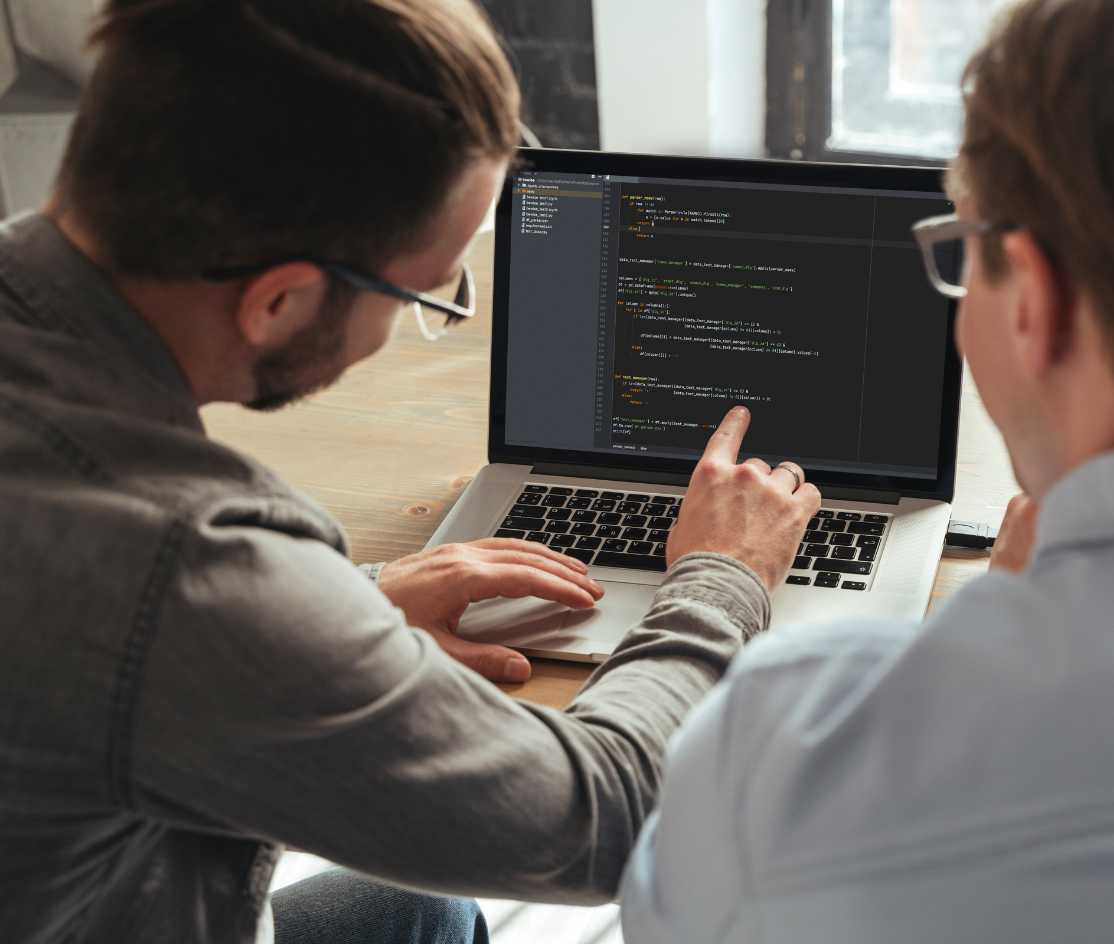 Deux développeurs discutant et pointant du code affiché sur un ordinateur portable.