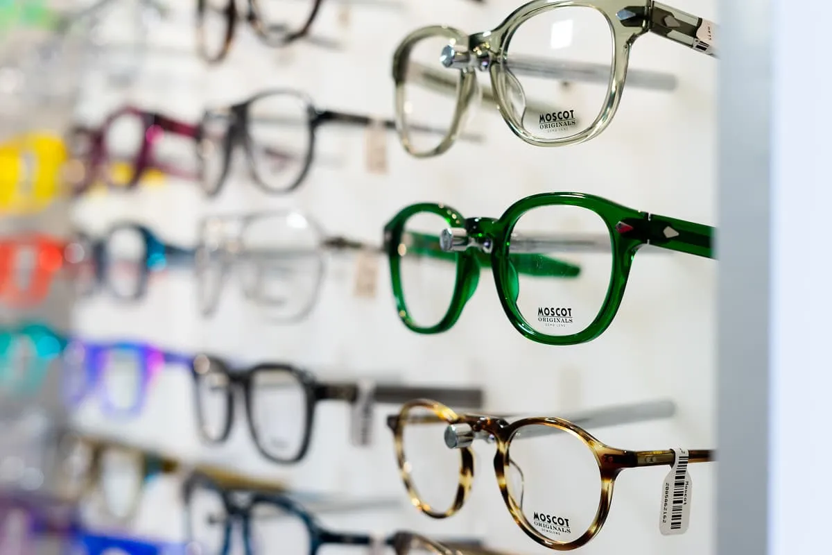 Multiple rows of varied sunglasses displayed on illuminated yellow shelves in an optometrist store.