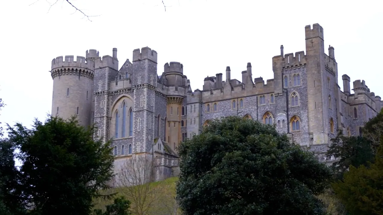 Large stone castle with turrets and battlements surrounded by trees on a grassy hill.