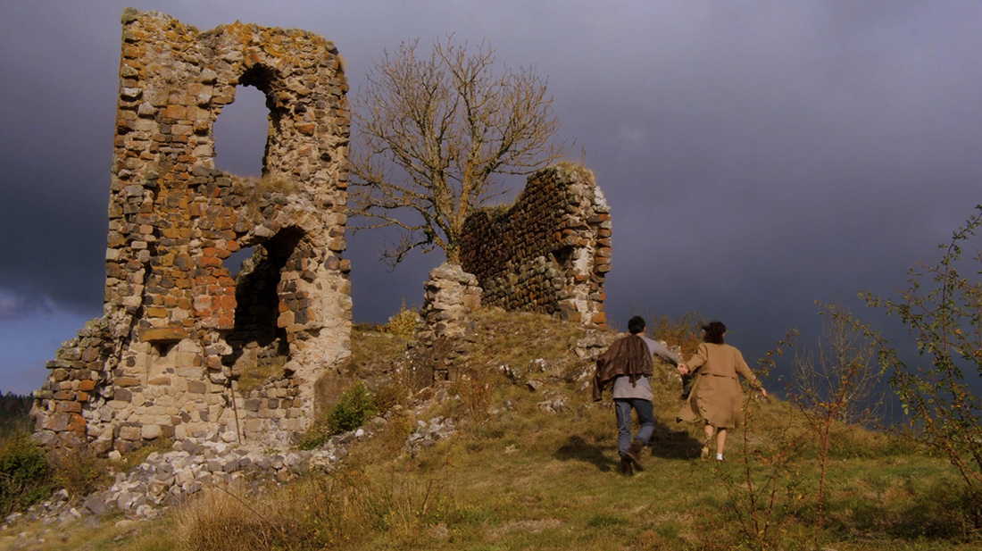 Two people walking up a hill with ruins.