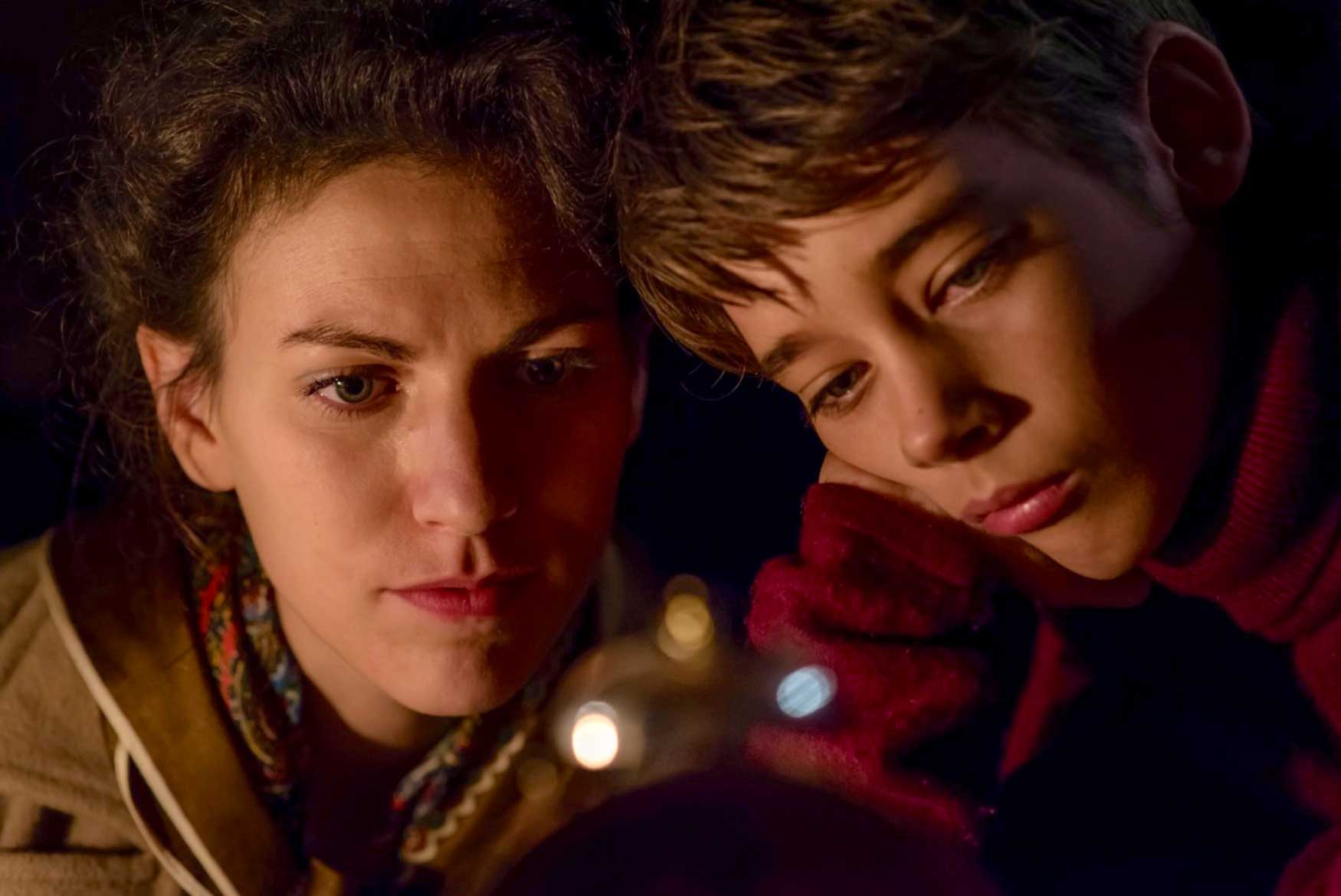 A woman with a boy looking at an object in the foreground.