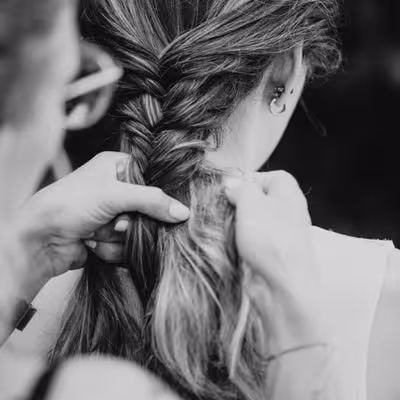 Nahaufnahme einer Person, die die Haare einer anderen Person zu einem Fischgrätenzopf flechtet.